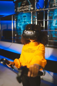 Child wearing VR goggles and using controllers in a tech-inspired indoor setting, enjoying a virtual reality game.