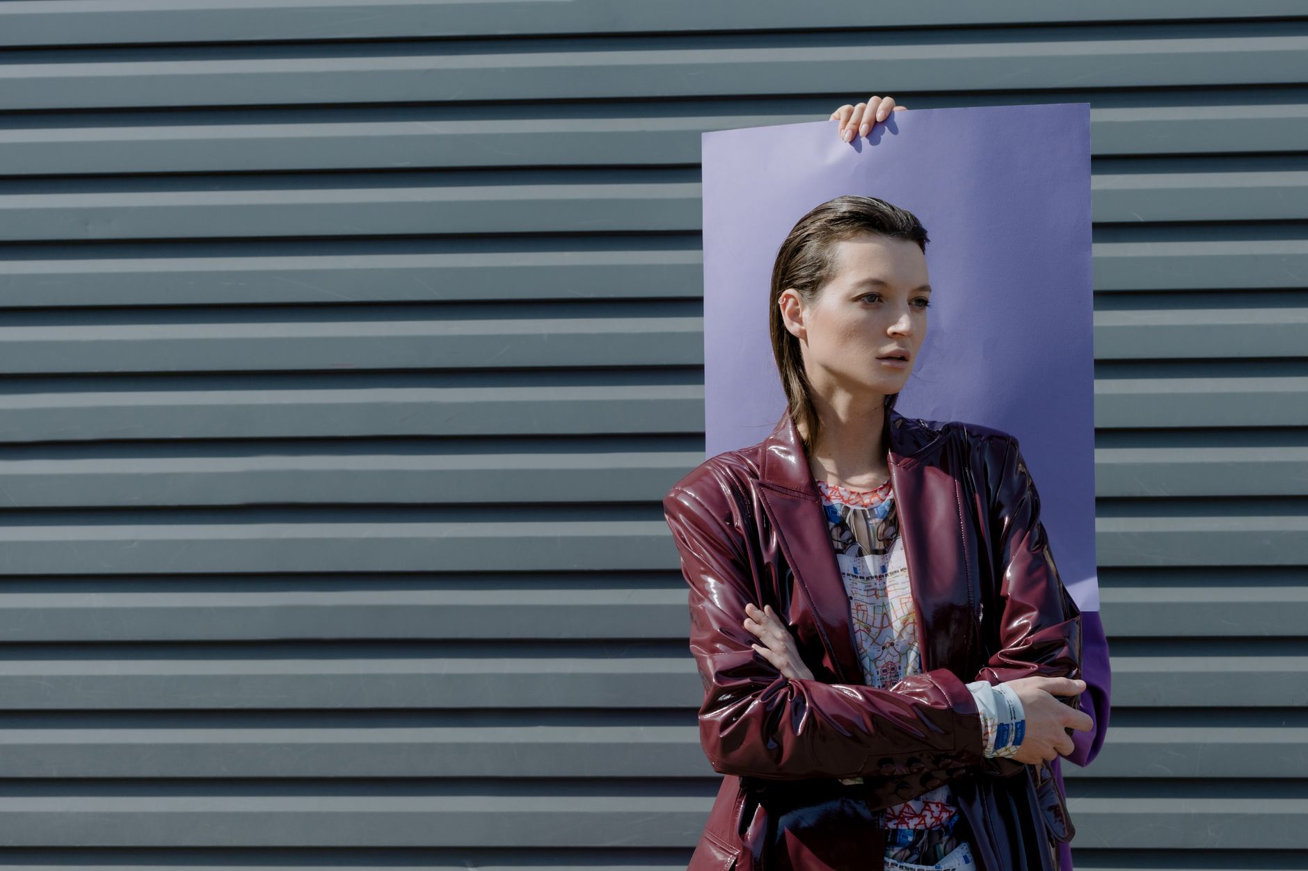 Fashionable woman in burgundy leather jacket posing against a modern background under daylight.