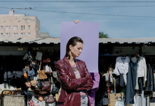 Stylish woman in leather coat posing confidently at an outdoor market, showcasing trendy fashion.