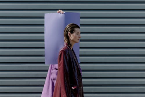 Woman in a Coat Standing Against a Piece of Paper and a Wall