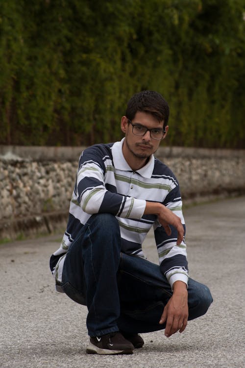 A Man Wearing Eyeglasses and Long Sleeve Shirt Sitting on the Concrete Pavement