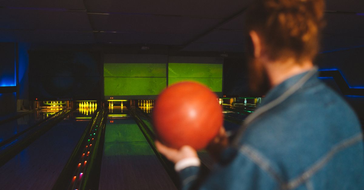 A man prepares to bowl in a neon-lit bowling alley, holding a red ball.