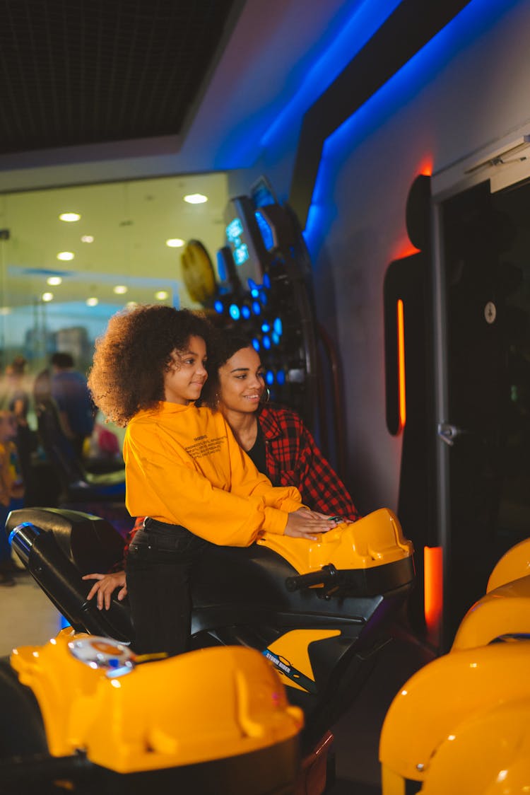 A Mother Beside A Girl Riding A Motorbike In Amusement Arcade 