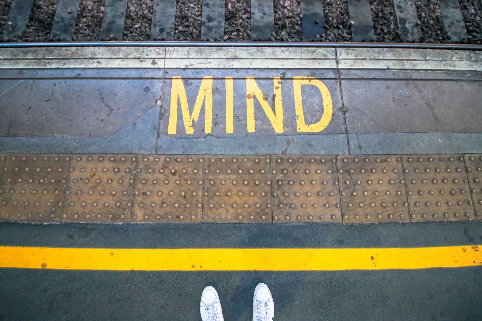 Close-up of railway platform edge with 'MIND' warning and yellow safety line, England.