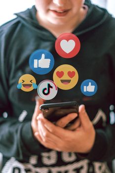 A teenager interacts with social media icons floating over a smartphone, illustrating digital connectivity and engagement.