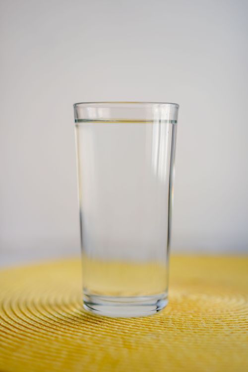 Free A tall clear glass filled with water on a textured yellow surface. Stock Photo