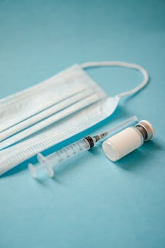 Close-up of a surgical mask, syringe, and vial on a blue surface, representing healthcare essentials.