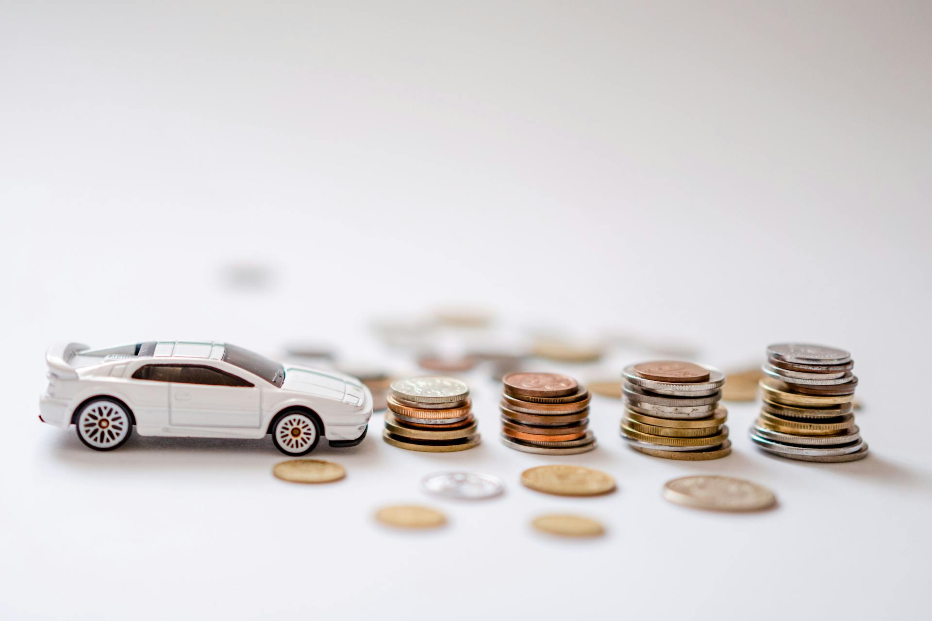 White toy sports car beside stacks of coins on a white background, emphasizing savings and finance.