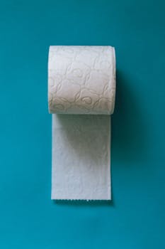 Vertical shot of a toilet paper roll against a vibrant blue backdrop.