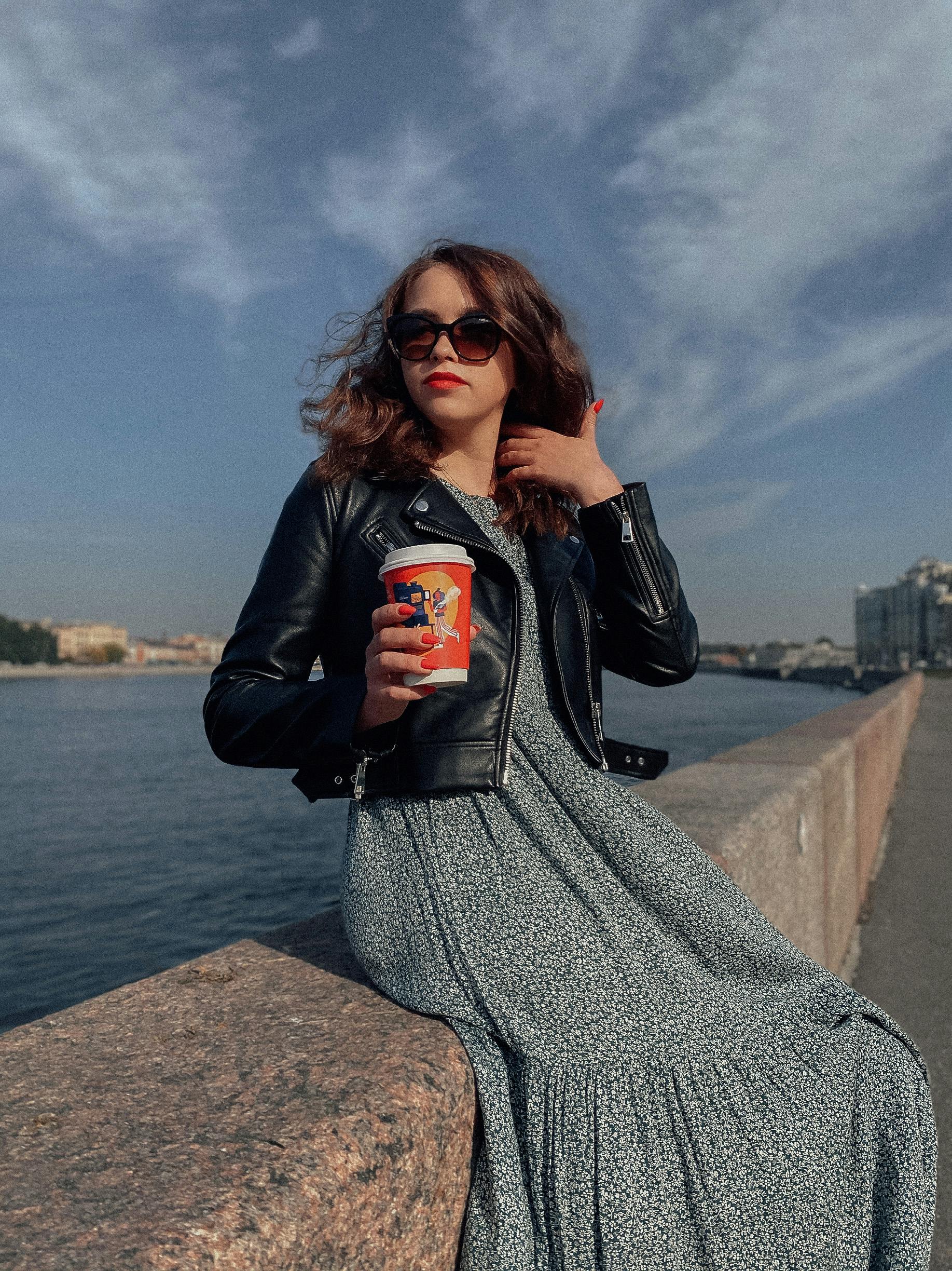 Fashionable woman enjoying a drink by the sea on a sunny day.