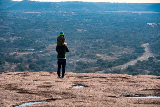 A father carries his daughter on his shoulders, enjoying the scenic Texas landscape from a high vantage point.