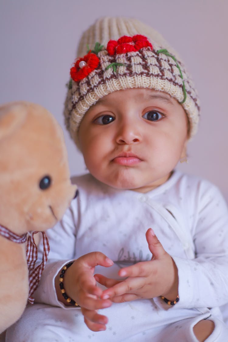 A Baby With Knitted Beanie Beside A Plush Toy Bear