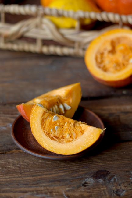 A whole mottled green and orange calabaza squash next to a wedge cut open showing dense orange flesh and seeds