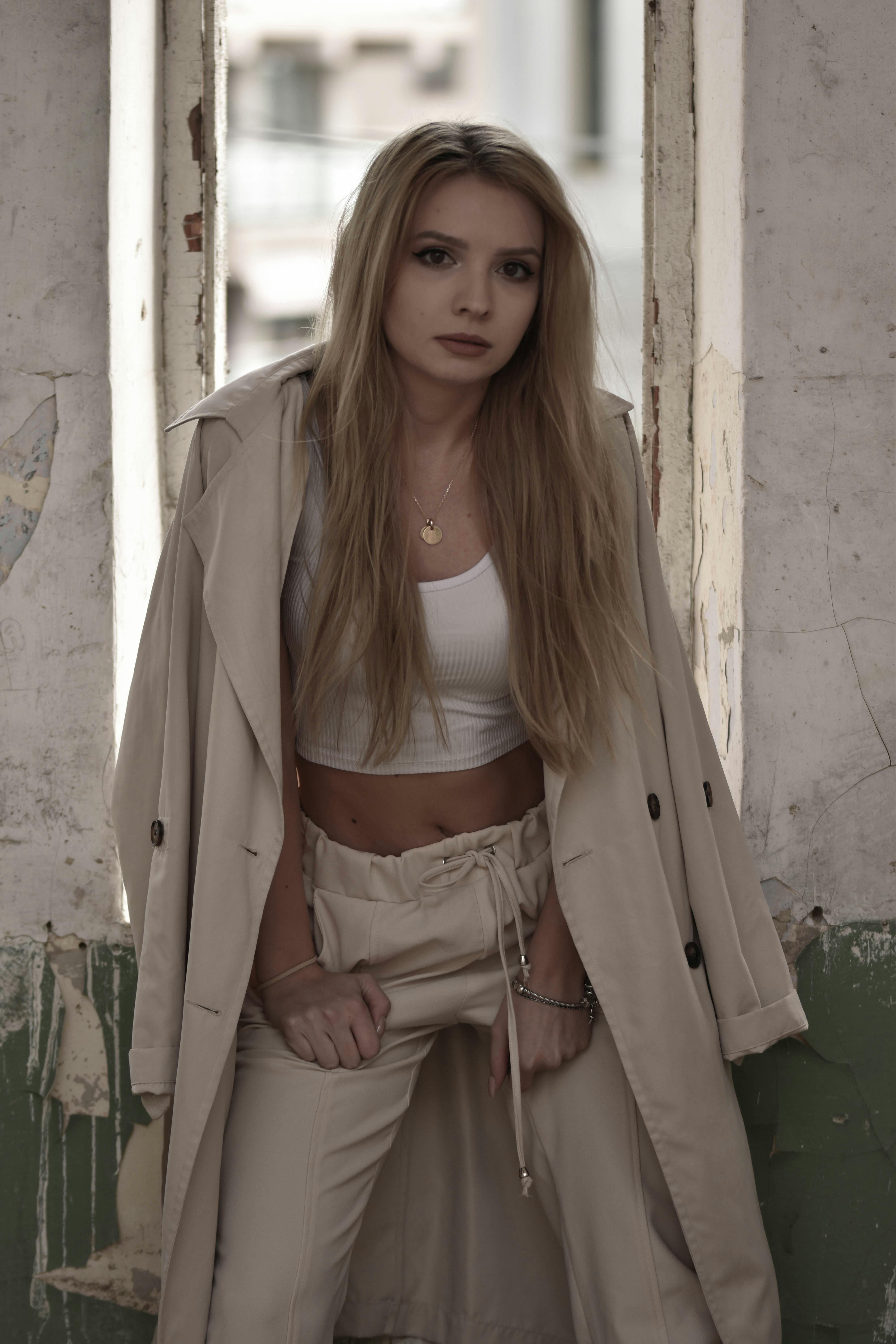 Fashionable woman in a beige trench coat standing indoors with natural lighting.