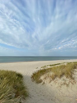 Peaceful dunes and open sea with a dramatic cloudy sky on a calm day.