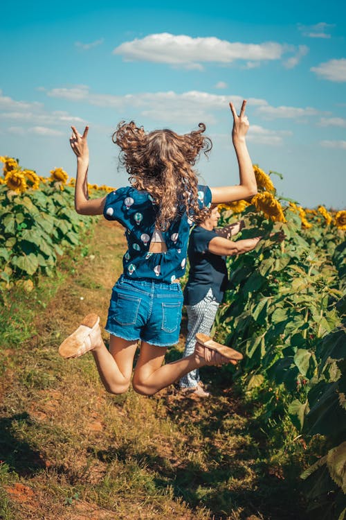 Woman in Blue Denim Shorts and Blue Shirt Jumping on Yellow Flower Field