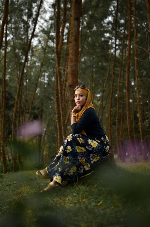 Free A woman sits in a serene forest wearing a floral dress, surrounded by trees. Stock Photo