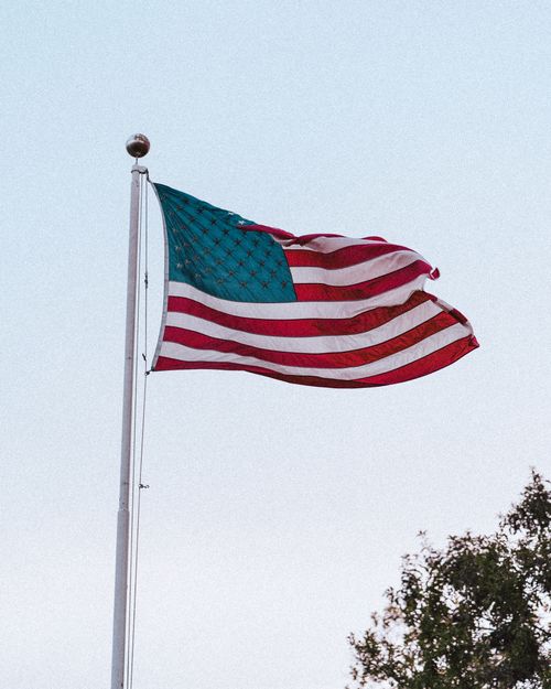 Free Close-up of the American flag waving on a flagpole with a clear sky backdrop. Stock Photo