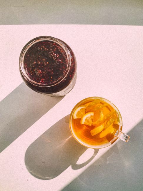 Aesthetic top view of lemon tea and berry jam on a sunlit surface, casting long shadows.