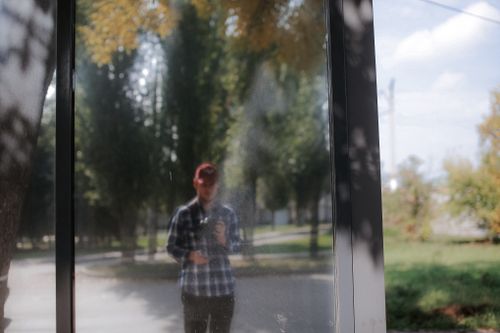 Free A man's reflection in a glass window with a street and trees visible outside. Stock Photo