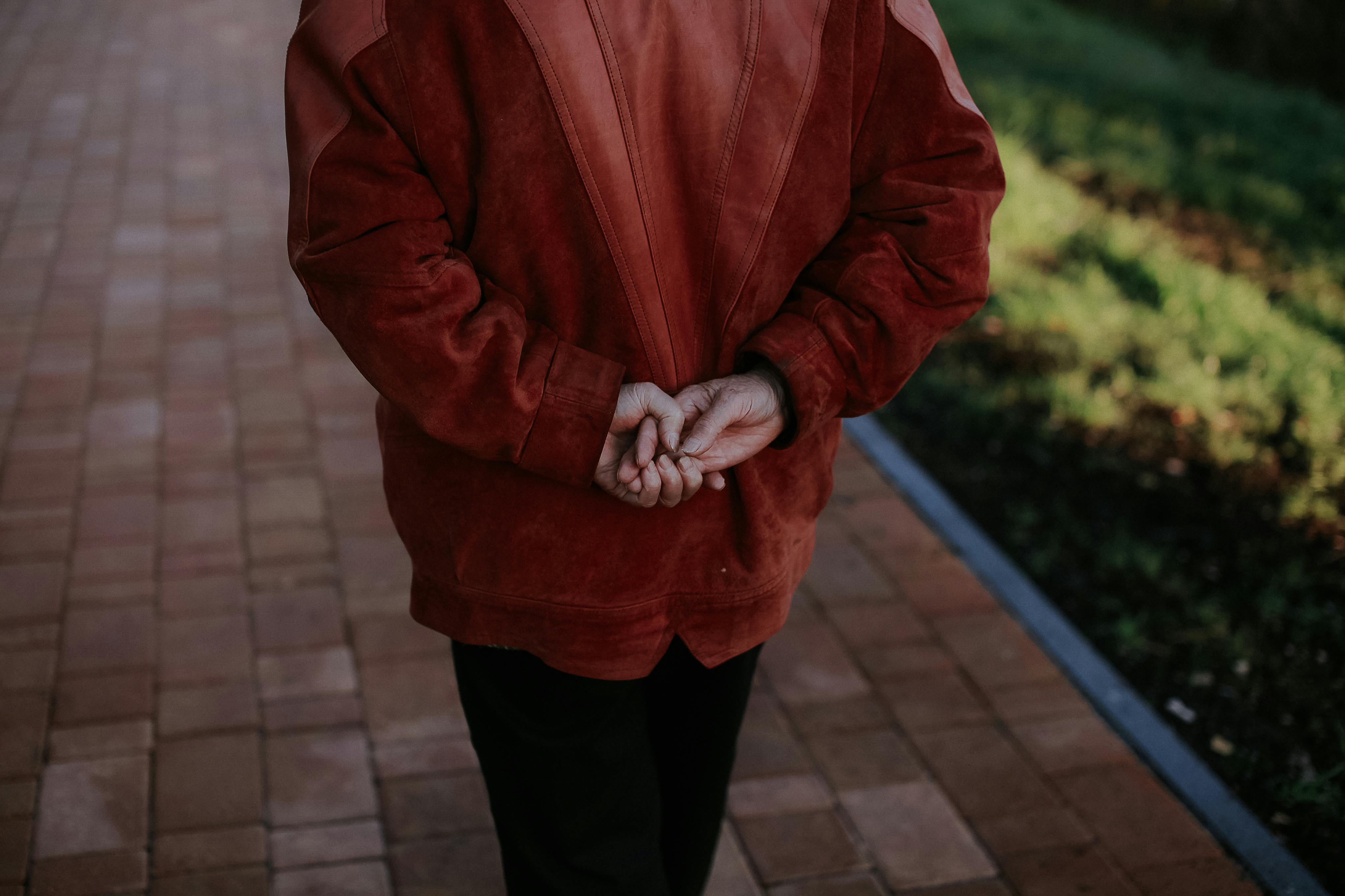 A senior woman leisurely walks on a brick pathway with hands behind her back.