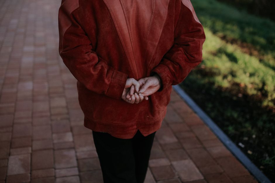 A senior woman leisurely walks on a brick pathway with hands behind her back.