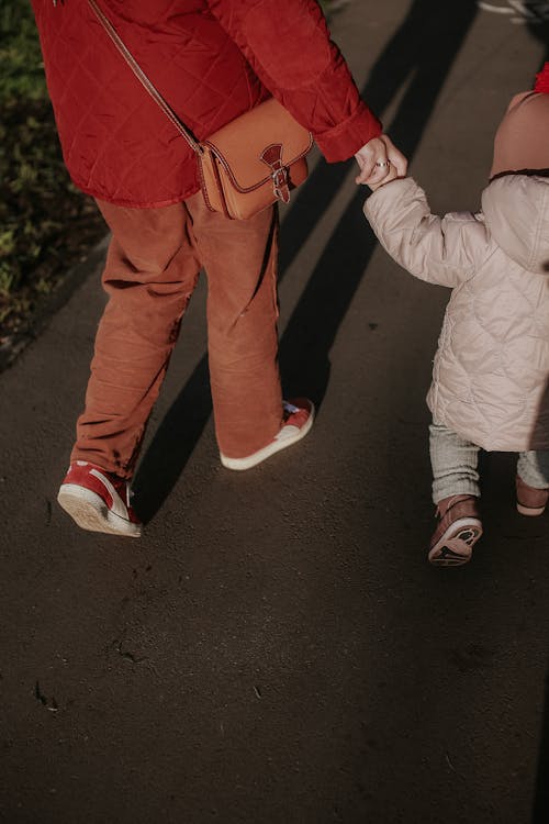 A Person in Red Jacket Holding the Hand of a Child While Walking