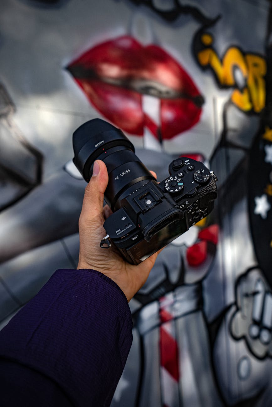Close-up shot of a hand holding a camera with graffiti in the background.