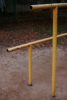 Close-up of rusty yellow bars in an outdoor playground with a dirt ground.