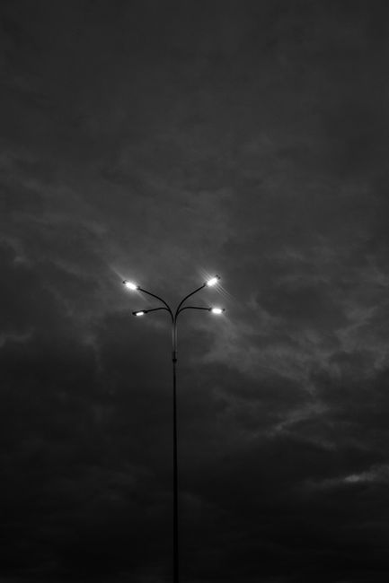 A solitary streetlight illuminates against a dark, cloudy night sky, creating a dramatic atmosphere.