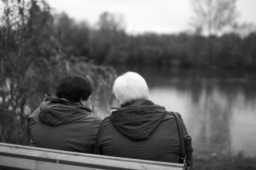 Free Two women sitting on a bench by the lake enjoying a serene moment. Stock Photo