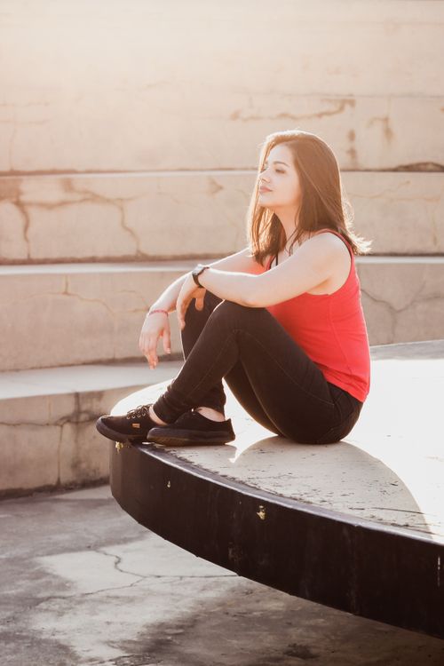 Free A woman in casual attire sitting on a concrete structure with sunlight casting soft hues. Stock Photo