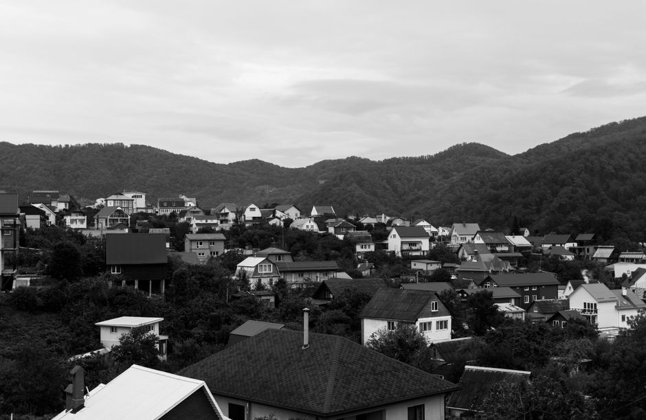 Black and white aerial shot of a village nestled in a valley surrounded by mountains.