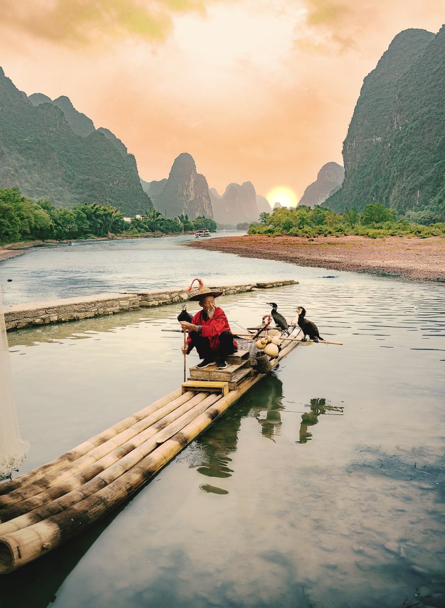 Pescador com cormorões numa jangada de bambu no rio Li, ao pôr do sol