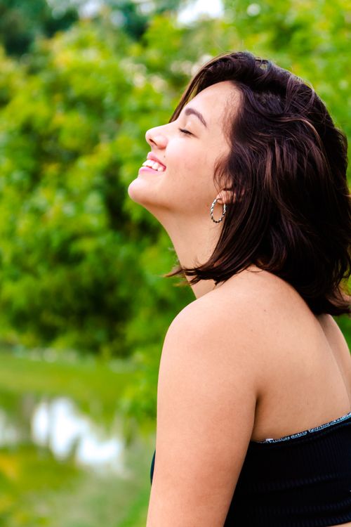 Free A joyful woman with short brunette hair smiles outdoors in a park, surrounded by lush greenery. Stock Photo