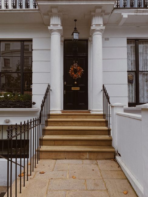 Charming townhouse entrance with columns, a black door, and autumn wreath.