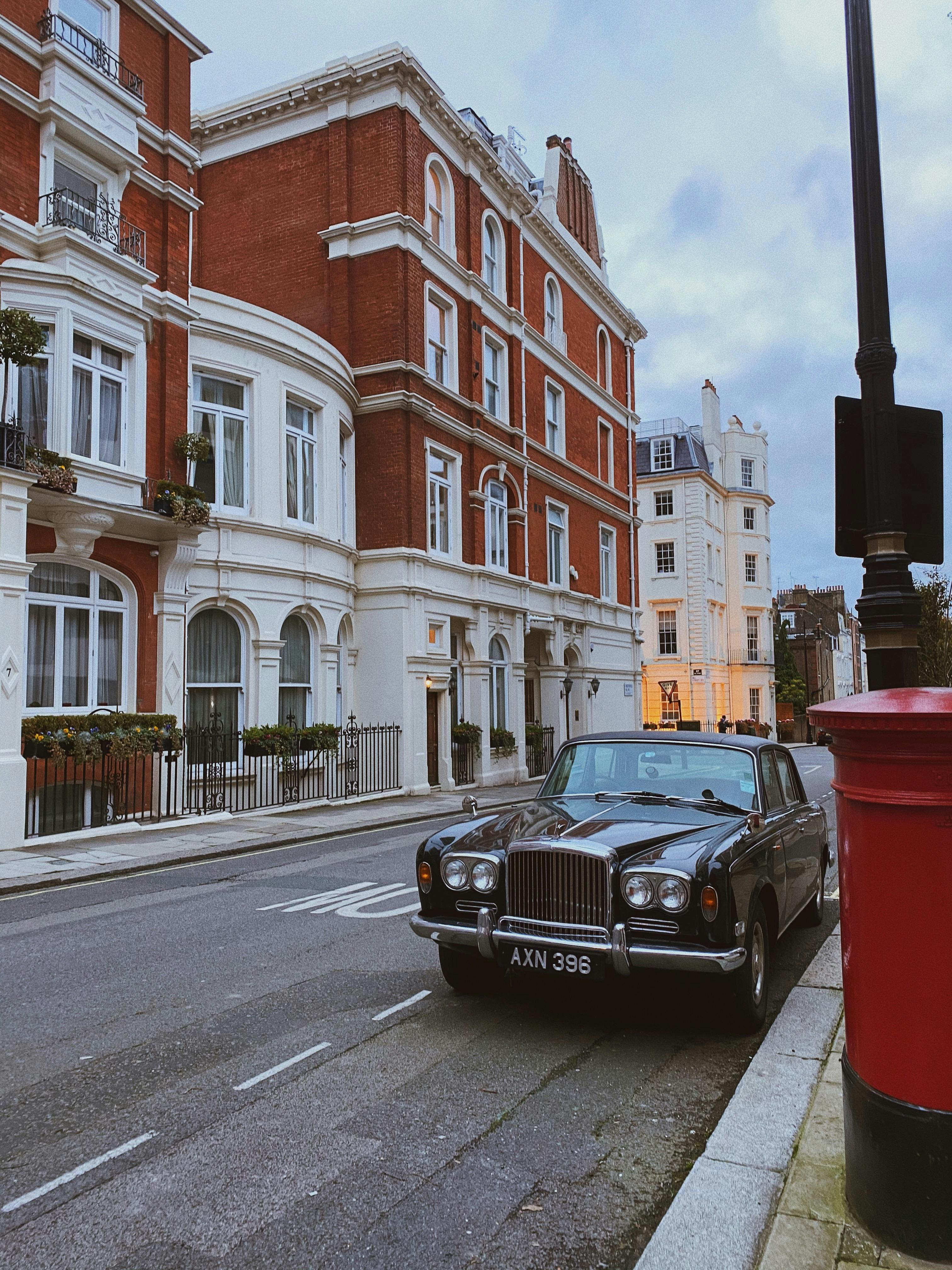 A classic black car parked on an empty London street with elegant brick buildings. Evening light sets a serene mood.