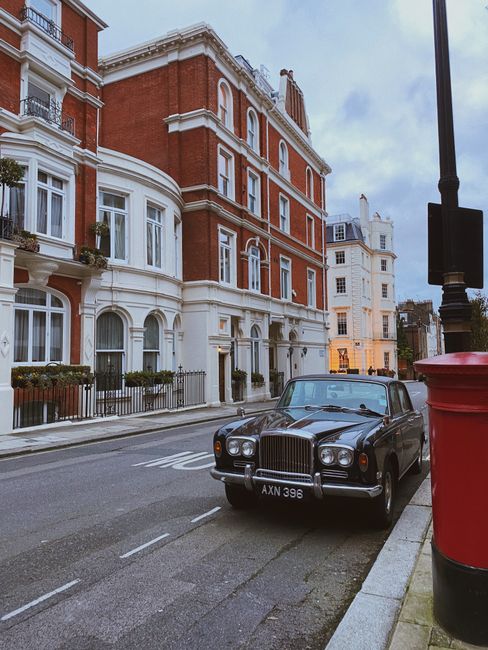 A classic black car parked on an empty London street with elegant brick buildings. Evening light sets a serene mood.