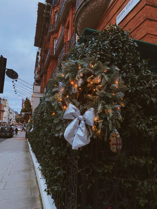 Free Elegant Christmas wreath with lights on a fence, capturing urban holiday spirit on a city sidewalk. Stock Photo