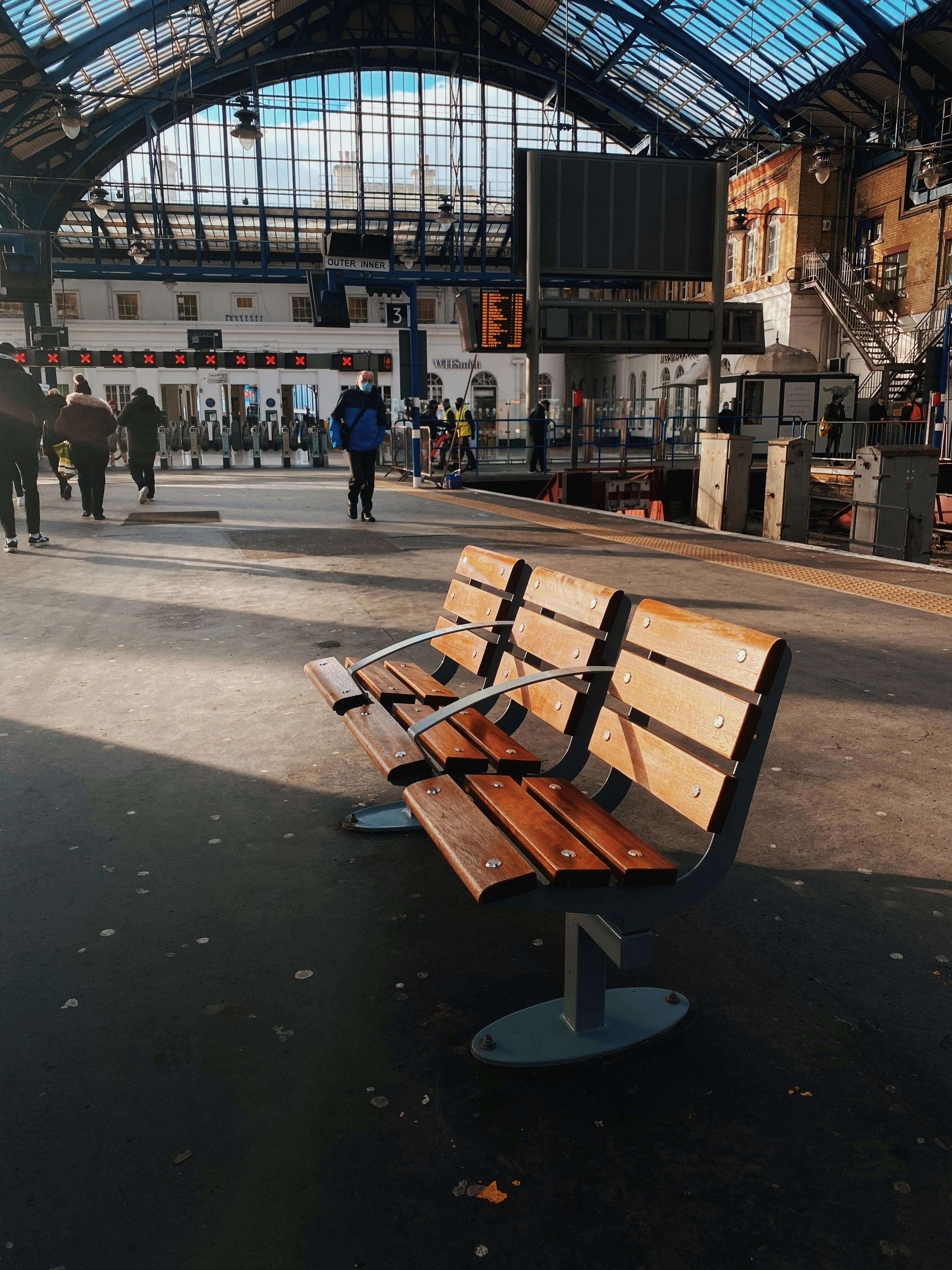 Empty wooden bench at Brighton Station with people in the background during daytime.