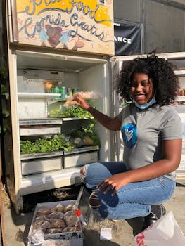 Smiling woman stocks a community fridge with fresh greens and groceries outdoors.