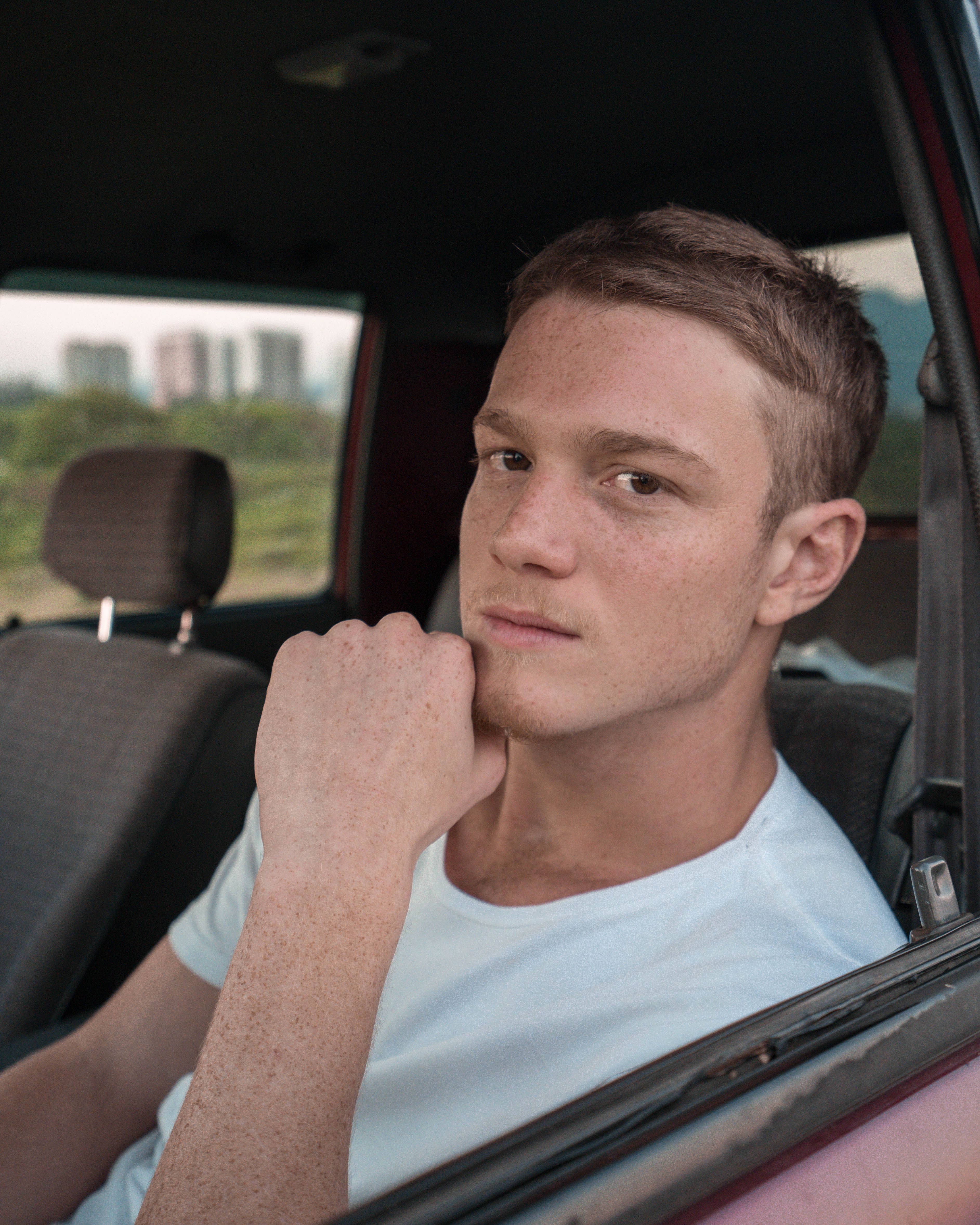 Caucasian man sitting thoughtfully in a car, looking out the window during the day.