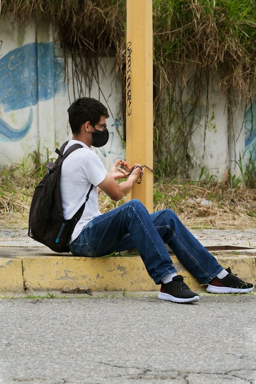 A Man in White Shirt Sitting on the Street while Wearing Face Mask