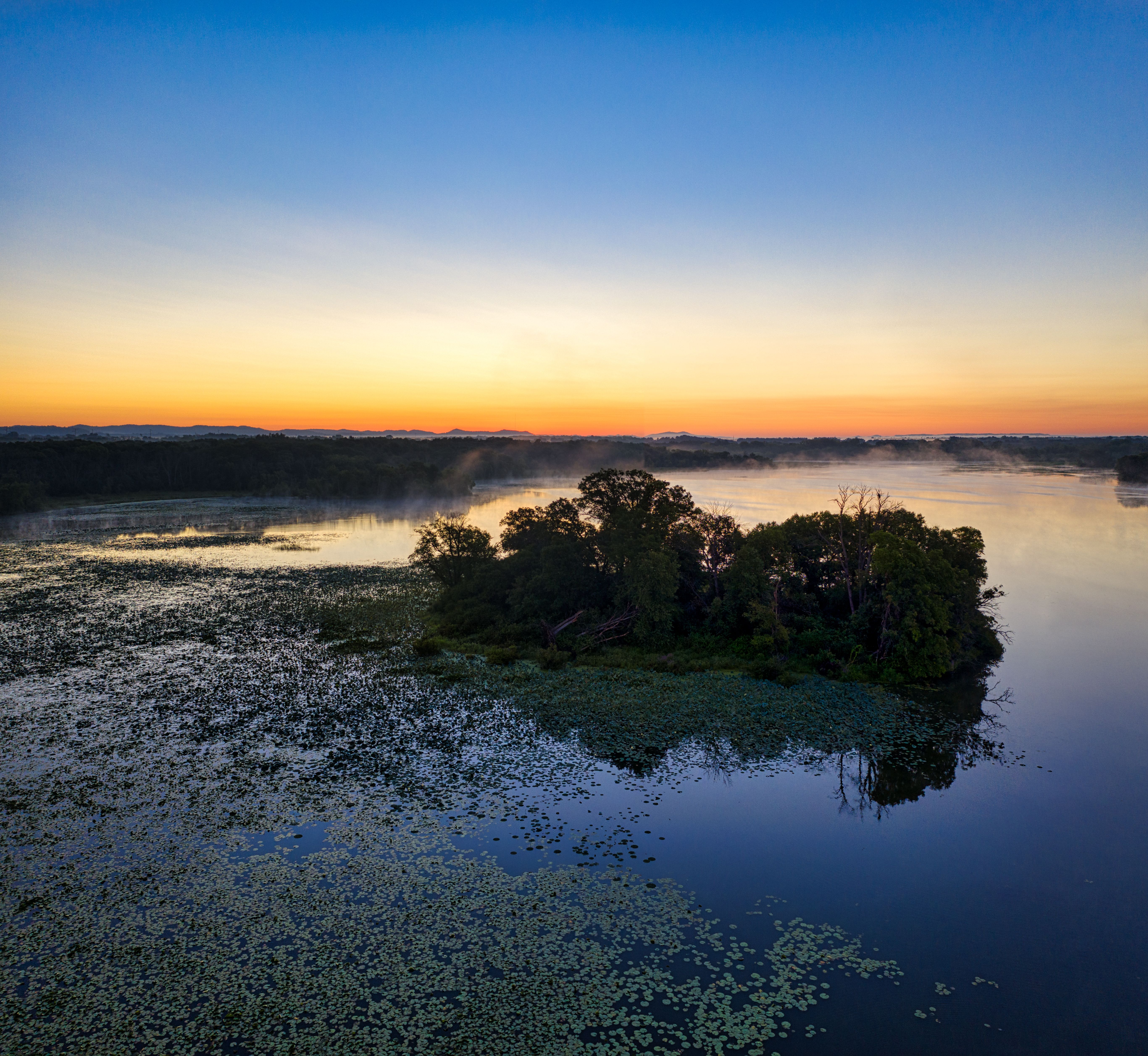 Captivating sunrise view of Trempealeau Lake with misty reflections and lush greenery.