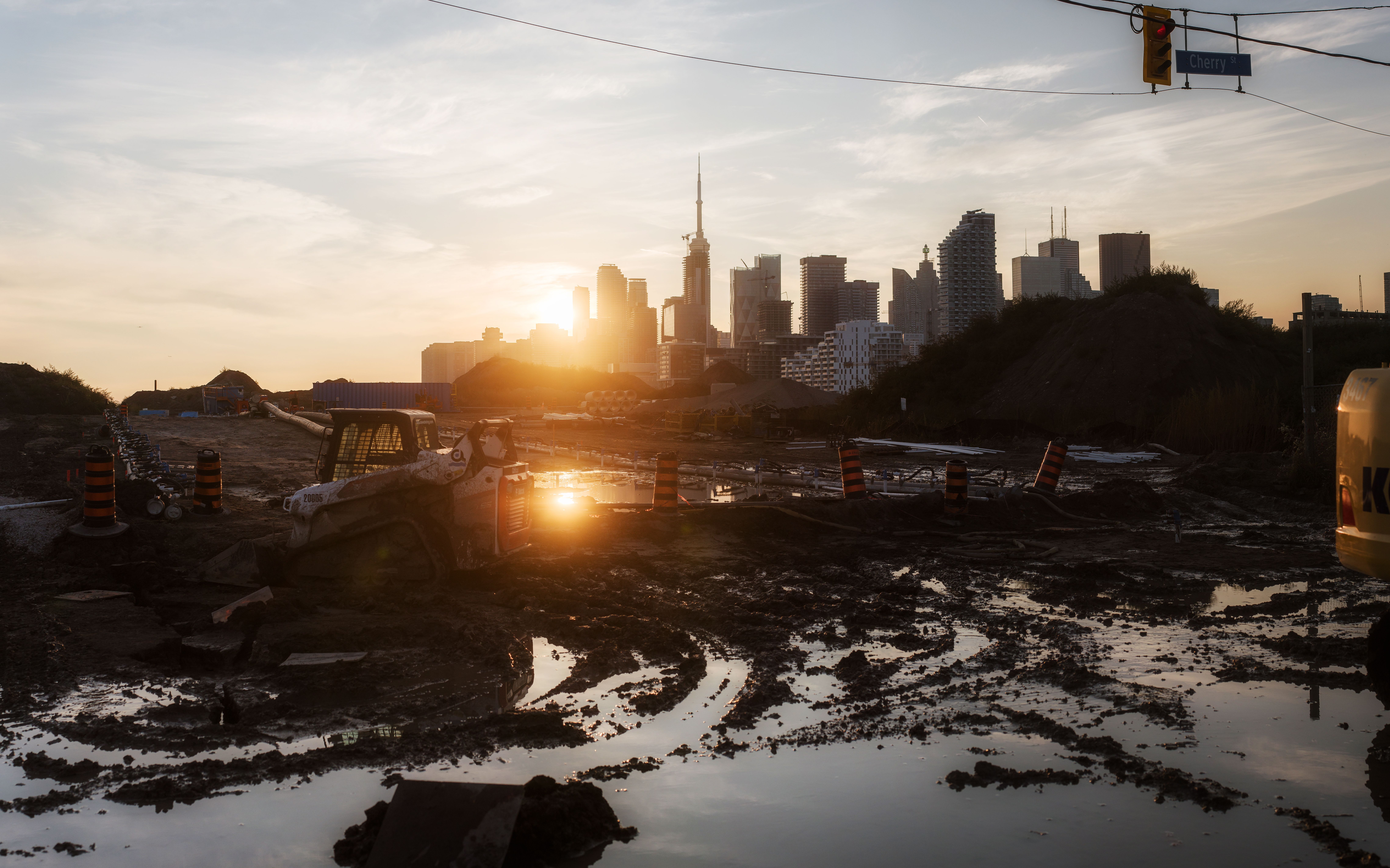 A tractor at a construction site with city skyline and sunset background, reflecting urban development.