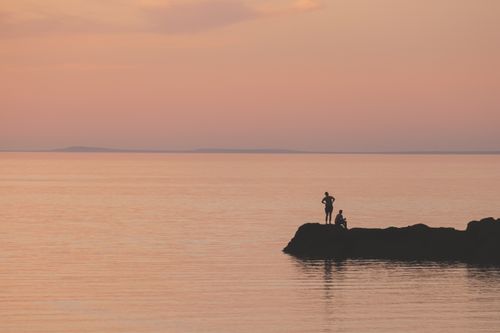 Free Two people silhouetted against a peaceful sunset by the sea, evoking tranquility and calm. Stock Photo
