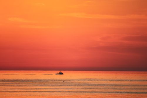 Free A tranquil sunset over the ocean with a silhouetted ship, featuring warm orange skies. Stock Photo