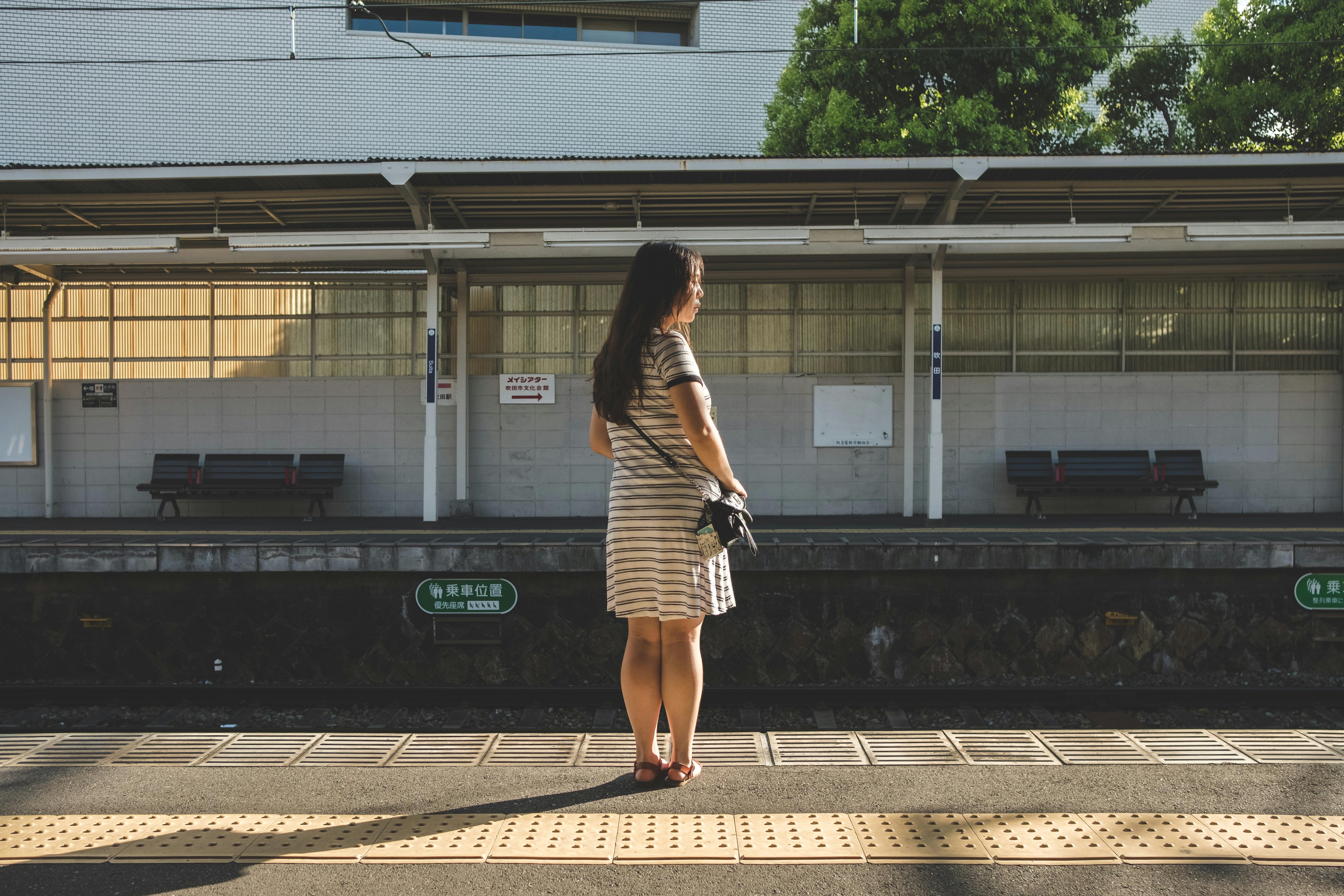 A woman in a striped dress awaits a train at an Osaka station during golden hour.