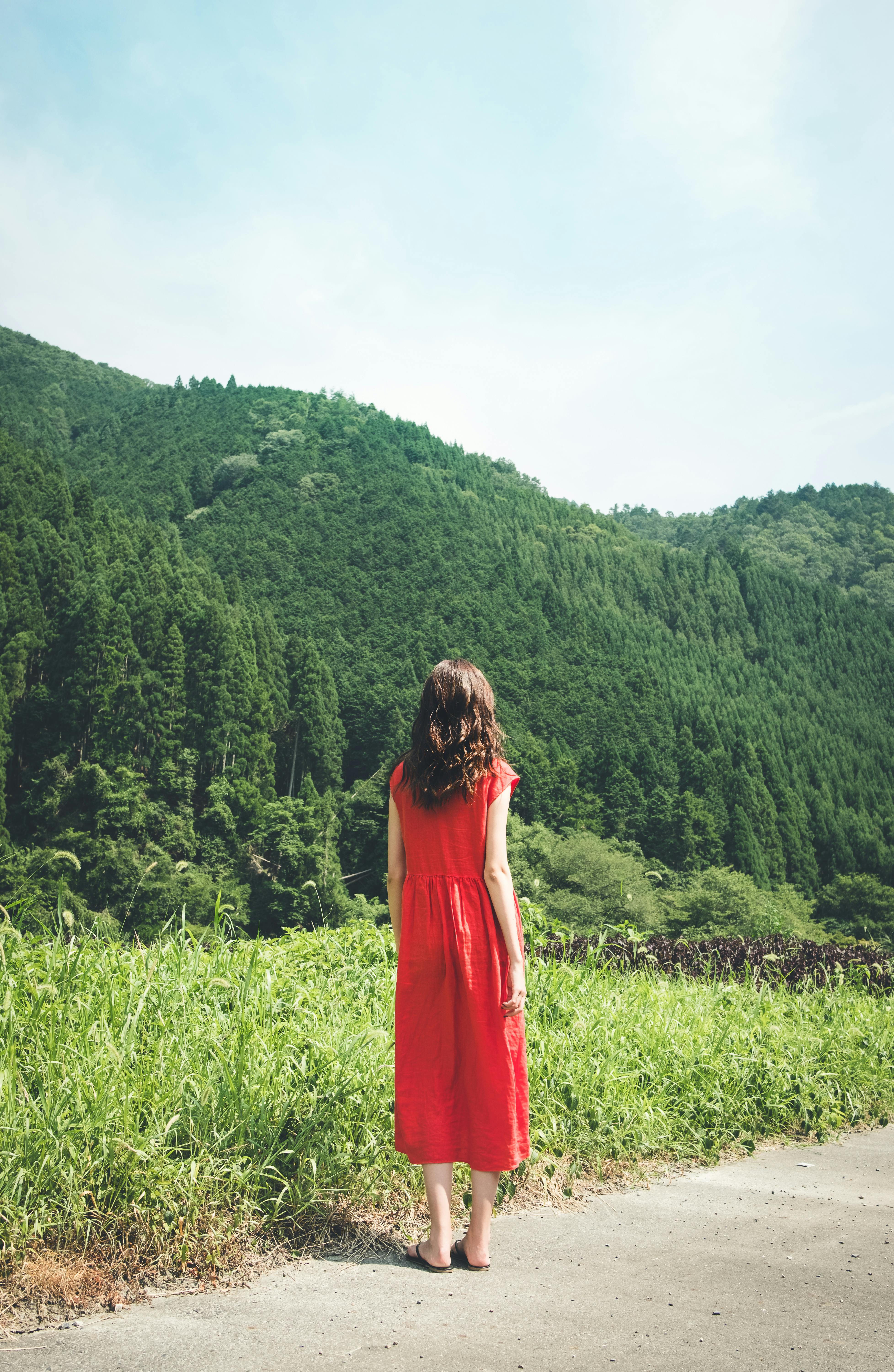 A woman in a red dress stands facing lush green mountains in Kyoto, Japan. Tranquil scene.