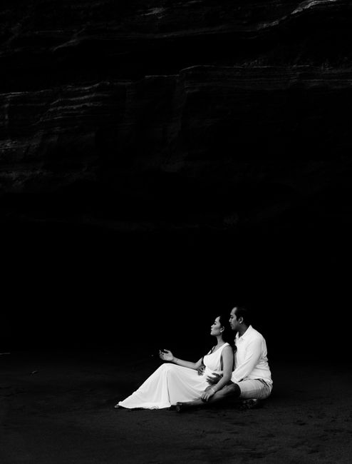 A couple in elegant attire sitting peacefully in a dark environment, captured in black and white.
